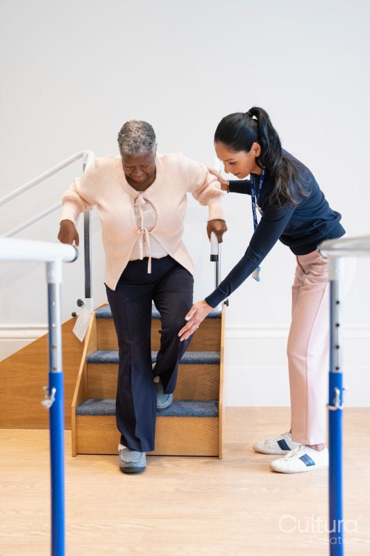 Female therapist assisting senior woman descending steps in exercise room