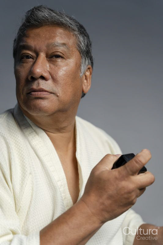 Portrait of serious man putting on perfume against gray background