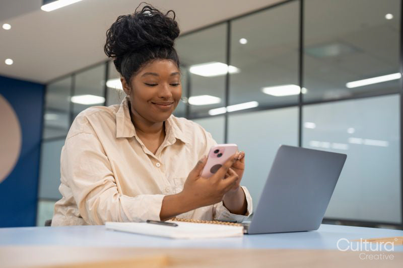 Businesswoman using phone and laptop in office