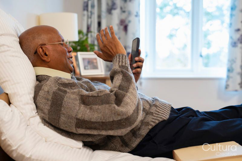 Senior man during video call on phone while lying on bed in his room at nursing home