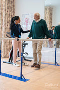 Female therapist assisting senior man walking on bars in exercise room