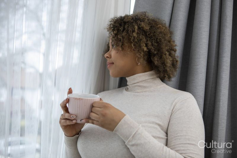 Woman with coffee cup looking through window