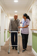 Care giver assisting senior man while walking along corridor in nursing home