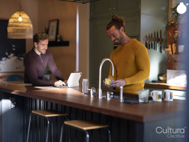 Man washing dishes while boyfriend using digital tablet at home kitchen