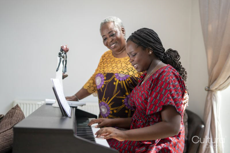Smiling woman assisting teenage granddaughter playing piano at home