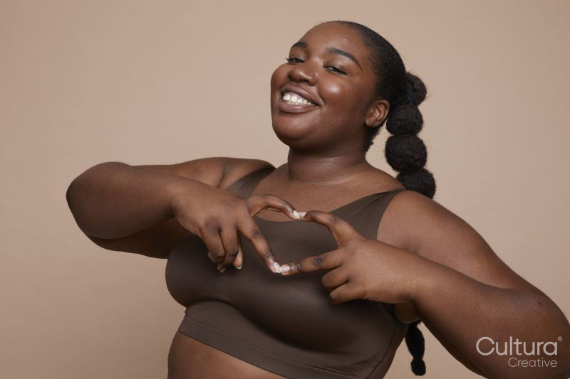 Studio portrait of smiling young woman with gesturing heart sign