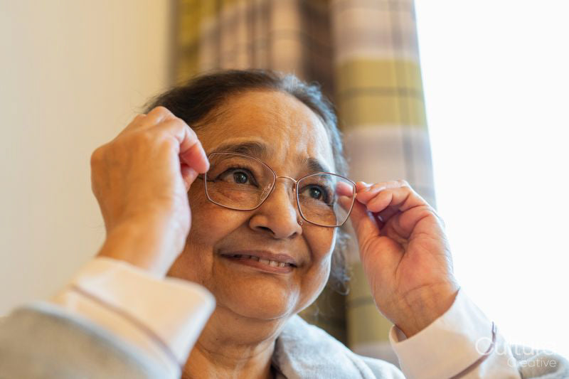 Senior lady putting on eyeglasses at nursing home