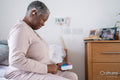 Senior woman in pajamas sitting on bed, holding pill organizer