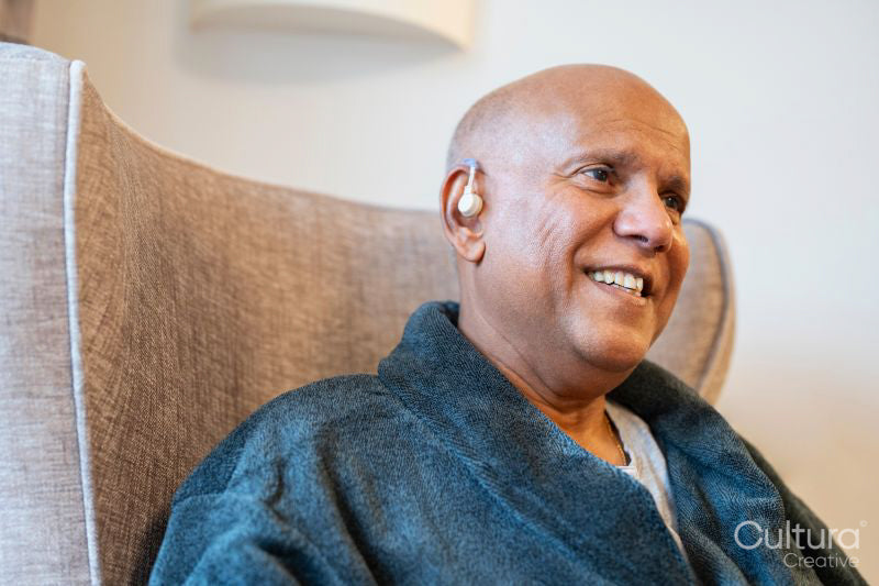 Senior man sitting in armchair with hearing aid in his room at nursing home