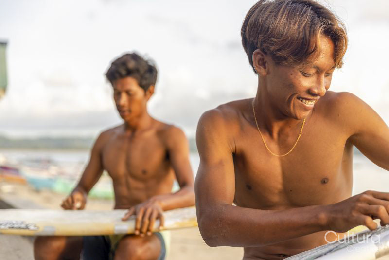 Surfers preparing surfboards on beach at sunset
