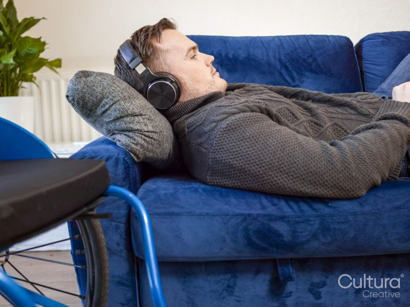 Man with headphones lying on sofa next to wheelchair