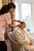 Nurse helps senior lady putting on hearing aid at nursing home