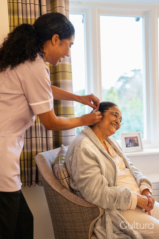 Nurse helps senior lady putting on hearing aid at nursing home