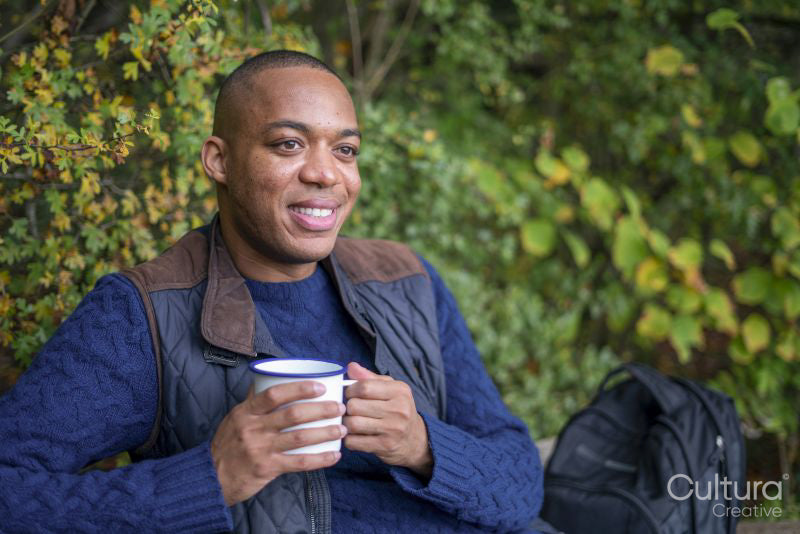Smiling man having warm drink during hike in autumn
