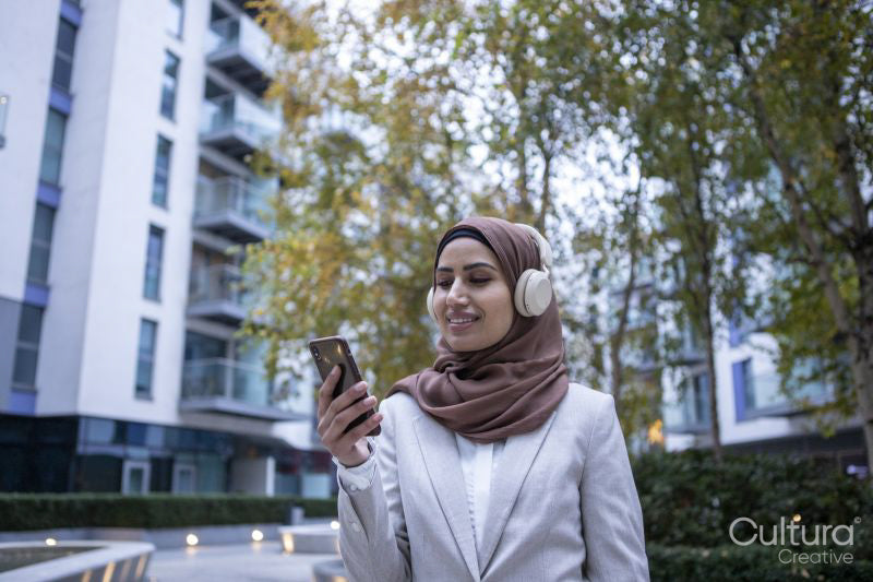 Businesswoman in hijab and headphones looking at smart phone