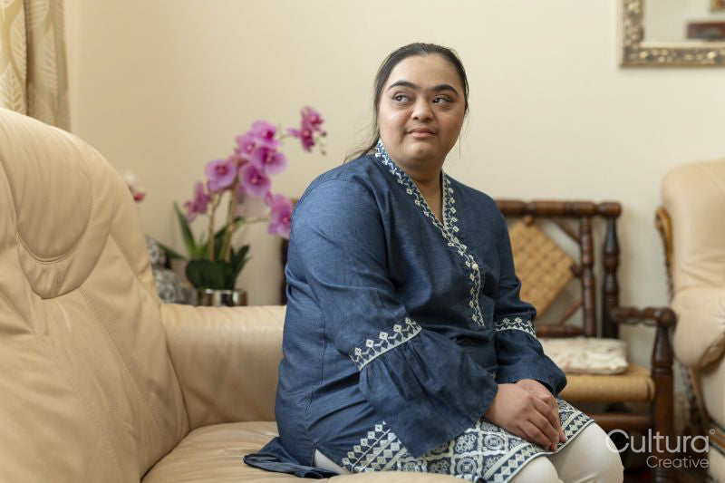 Portrait of young woman with down syndrome sitting on sofa at home