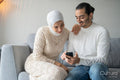 Mid adult couple sitting on sofa and using smart phone
