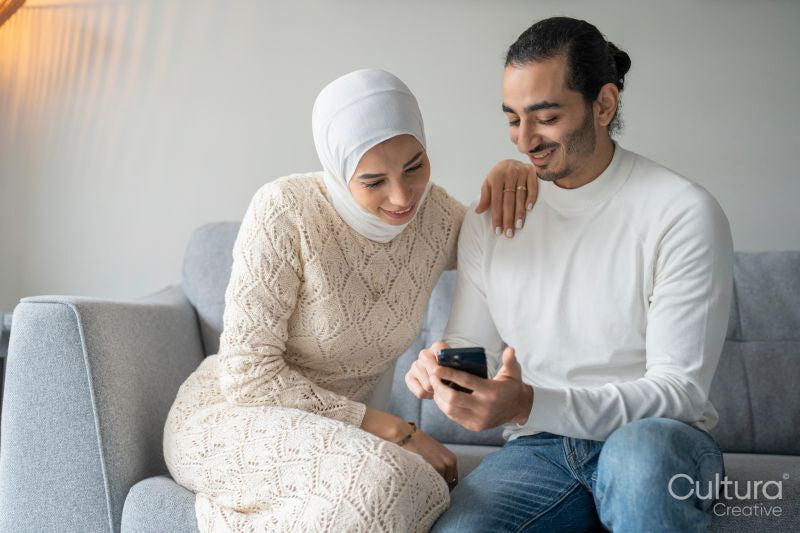 Mid adult couple sitting on sofa and using smart phone