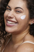 Close-up portrait of young woman applying face cream
