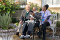 Smiling senior people accompanied by nurse relaxing in park and looking at phone