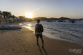 Rear view of man with backpack on beach at sunset