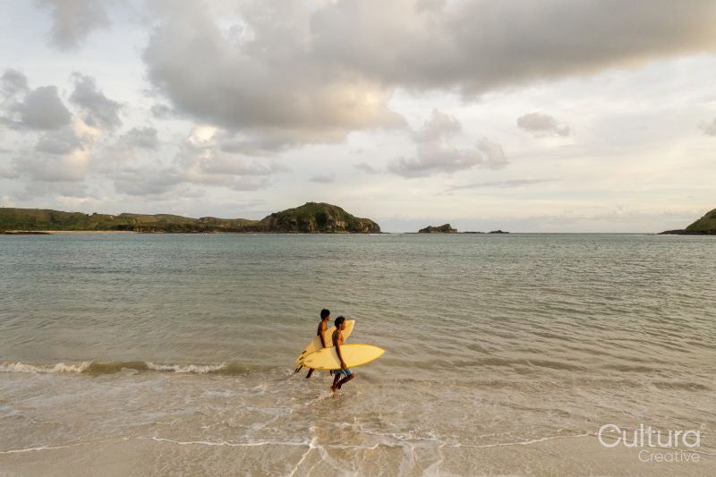Indonesia, Lombok, Side view of surfers walking in sea at sunset