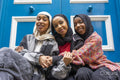 Portrait of three smiling women wearing hijabs embracing in city