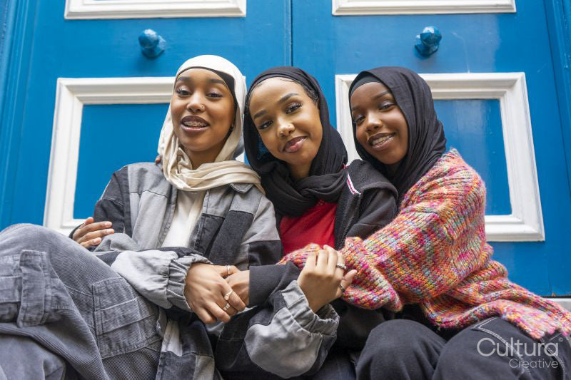 Portrait of three smiling women wearing hijabs embracing in city