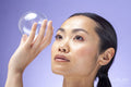 Close-up of woman holding soap bubble against purple background