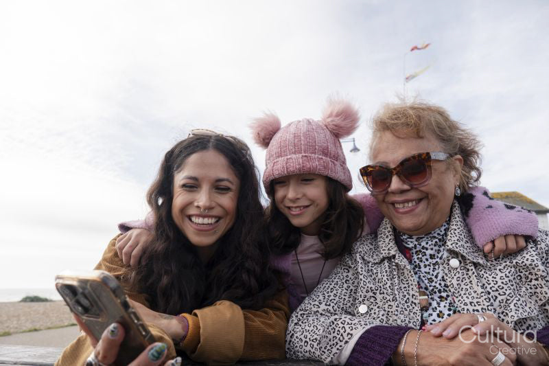 Grandmother, mother and daughter looking at smart phone on beach