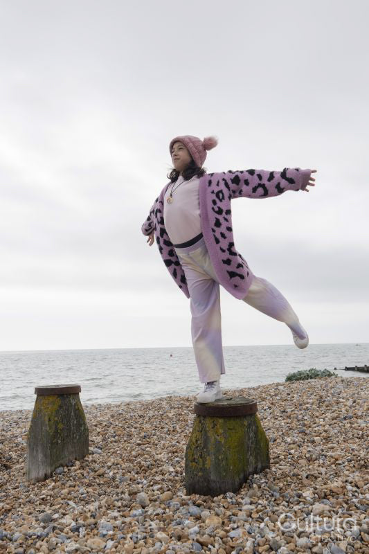 Girl standing on one leg on groyne with arms outstretched