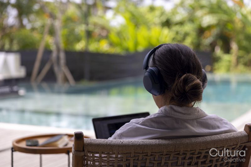 Rear view of woman using laptop with headphones at poolside