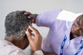 Caregiver assisting senior woman adjusting hearing aid