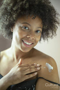 Portrait of smiling woman applying moisturizer on shoulder