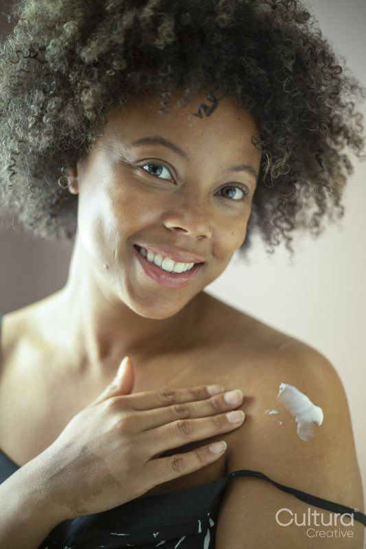 Portrait of smiling woman applying moisturizer on shoulder