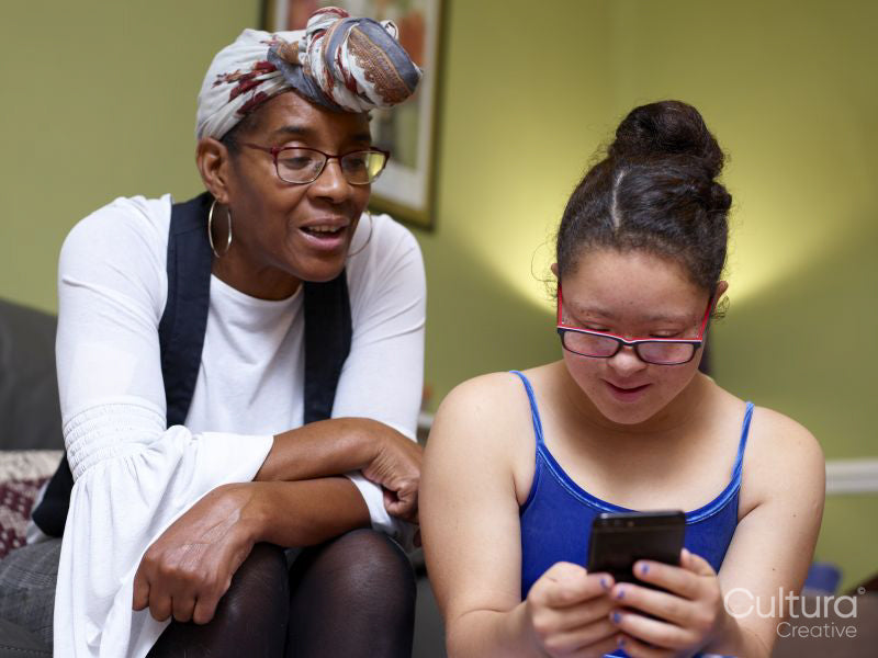 Mother with daughter with Down Syndrome looking at smart phone at home