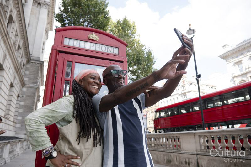Happy mature couple taking selfie in front of traditional red telephone booth
