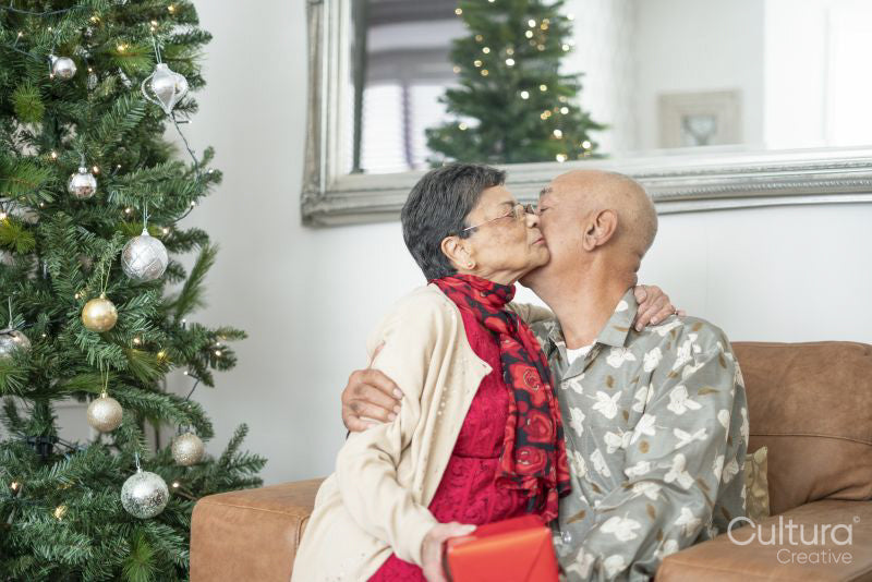 Senior couple holding gift and kissing at Christmas tree
