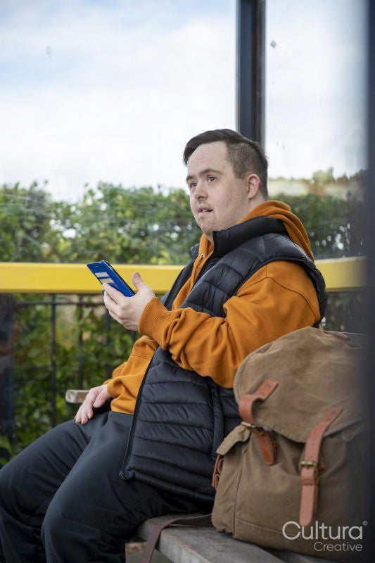 Man sitting on bench at bus stop, using smart phone