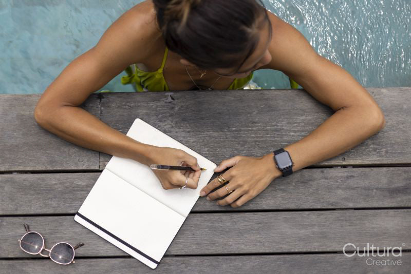 Woman writing in notepad while relaxing in swimming pool, overhead view