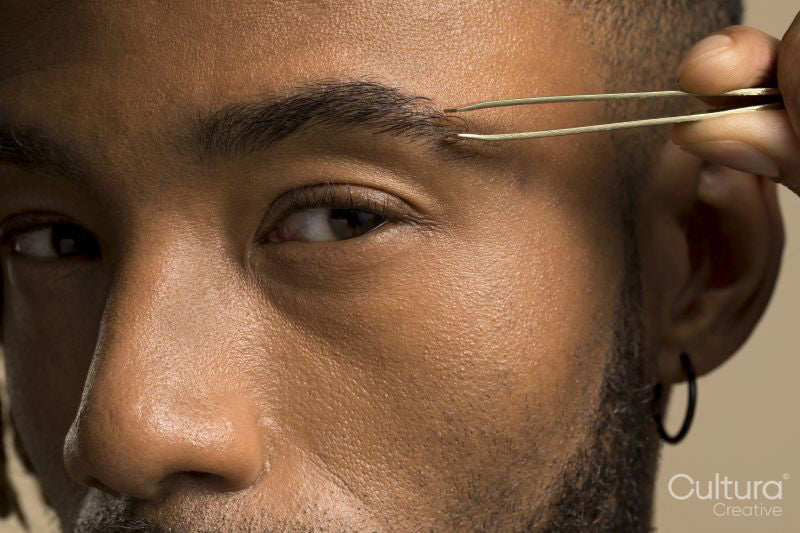 Studio portrait of young man plucking eyebrow