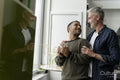 Mature male couple standing by window at home