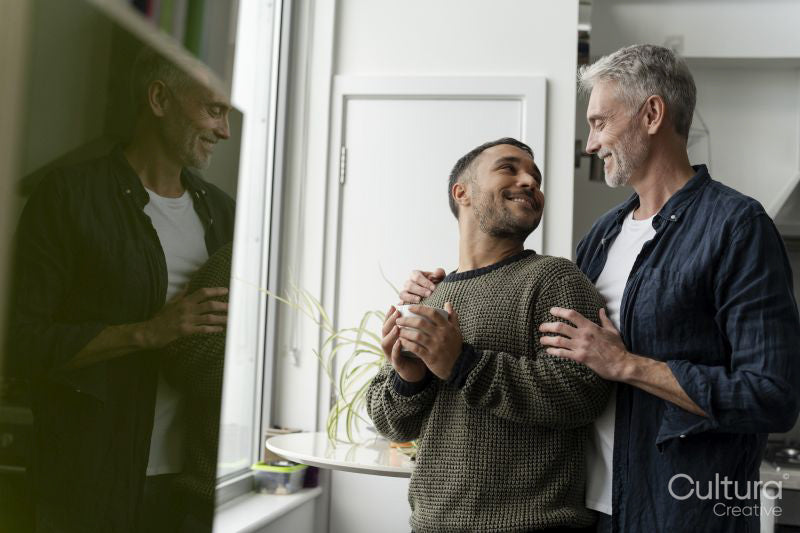 Mature male couple standing by window at home