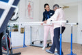 Smiling female therapist assisting senior woman walking on bars
