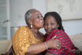 Smiling senior woman hugging and kissing teenage granddaughter at home