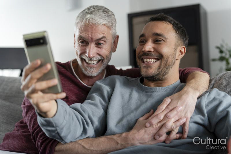 Smiling male couple taking selfie on sofa