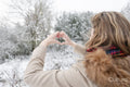 Rear view of woman making hand heart sign in winter landscape