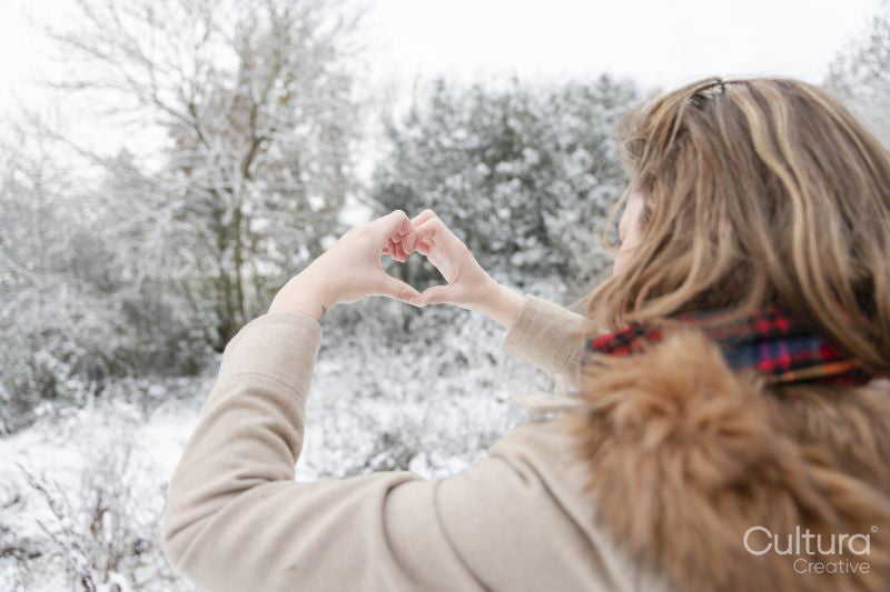 Rear view of woman making hand heart sign in winter landscape