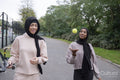 Two women in hijabs walking in park with tennis racket and ball