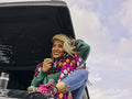 Woman sitting on roof of car drinking from insulated drink container